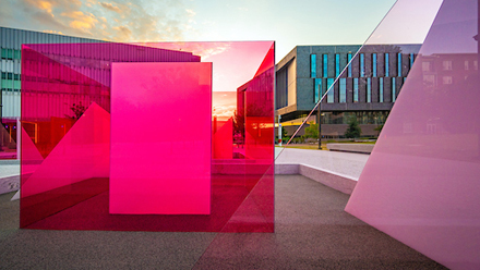 The sun sets on Centennial Campus behind the Hunt Library and the Reds and Whites art installation on the Engineering Oval.